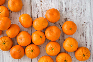 Small clementine oranges spilled onto a whitewashed wood background
