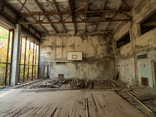 Abandoned empty gym in school in Pripyat near Chernobyl, Ukraine. The surrounding of the gym is overgrown with trees and bushes.