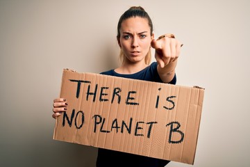 Young beautiful blonde woman with blue eyes asking for protect planet holding banner pointing with finger to the camera and to you, hand sign, positive and confident gesture from the front