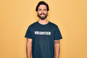 Young handsome hispanic volunteer man wearing volunteering t-shirt as social care with a happy and...