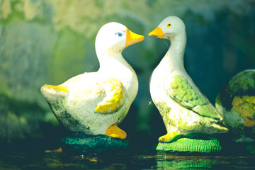 Two duck dolls on water in a pond with nature background.