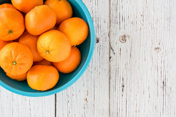 Small clementine oranges in a light blue bowl on a whitewashed wood background
