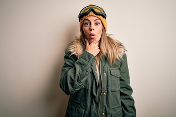 Young brunette skier woman wearing snow clothes and ski goggles over white background Looking fascinated with disbelief, surprise and amazed expression with hands on chin
