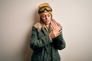 Young brunette skier woman wearing snow clothes and ski goggles over white background Suffering...