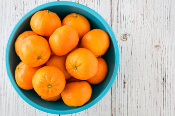 Small clementine oranges in a light blue bowl on a whitewashed wood background
