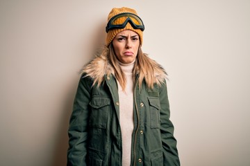 Young brunette skier woman wearing snow clothes and ski goggles over white background depressed and worry for distress, crying angry and afraid. Sad expression.