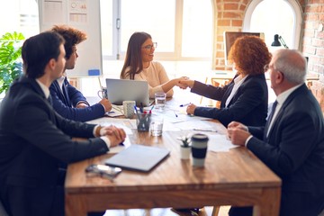 Group of business workers smiling happy and confident in a meeting. Speaking with smile on face working together shaking hands for agreement at the office.