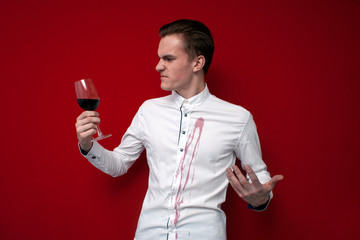 sad guy in a white shirt spilled red wine on himself on a red background, an angry man put a stain...