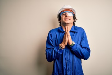 Young constructor man wearing uniform and security helmet over isolated white background begging and praying with hands together with hope expression on face very emotional and worried. Begging.