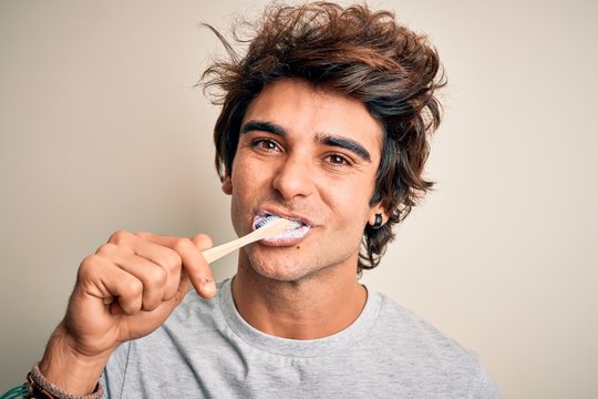 Young handsome man smiling happy. Standing with smile on face whasing tooth using toothbrush over isolated white background