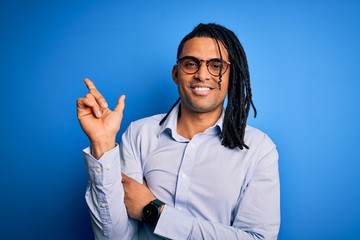 Young handsome african american man with dreadlocks wearing casual shirt and glasses with a big smile on face, pointing with hand and finger to the side looking at the camera.