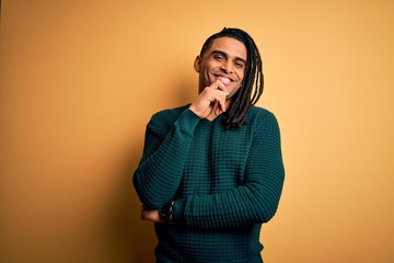 Young handsome african american afro man with dreadlocks wearing green casual sweater looking confident at the camera with smile with crossed arms and hand raised on chin. Thinking positive.