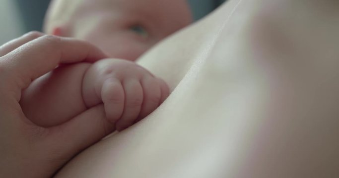 View of mom's hand caresses her baby's little palm at chest during breastfeeding