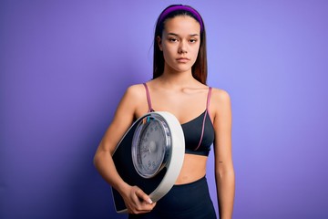 Young beautiful slim sporty girl doing sport wearing sportswear holding weight machine with a confident expression on smart face thinking serious