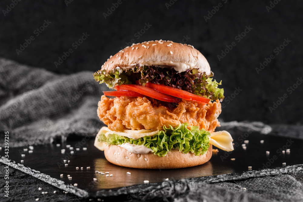 Wall mural chicken burger with cheese, tomatoes, lettuce and sauce on slate black background, close up