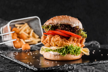 Chicken burger with cheese, tomatoes, lettuce, sauce and fried stick balls, french fries on slate...