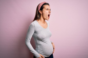 Young beautiful teenager girl pregnant expecting baby over isolated pink background angry and mad...