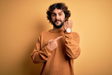 Young handsome man with beard wearing casual sweater standing over yellow background In hurry...