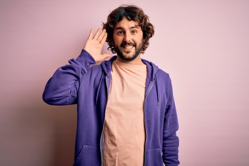 Young handsome sporty man with beard wearing casual sweatshirt over pink background Waiving saying hello happy and smiling, friendly welcome gesture