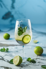 Fresh Mojito cocktail with lime, mint and ice in wineglass on light blue background. Studio shot of drink in freeze motion, drops. Summer cold drink and cocktail