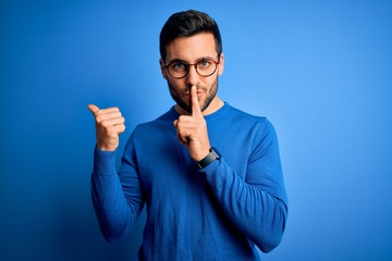 Young handsome man with beard wearing casual sweater and glasses over blue background asking to be...