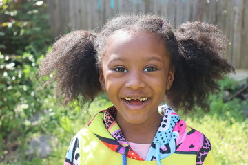 Happy African American girl missing two front teeth outdoors - obrazy, fototapety, plakaty