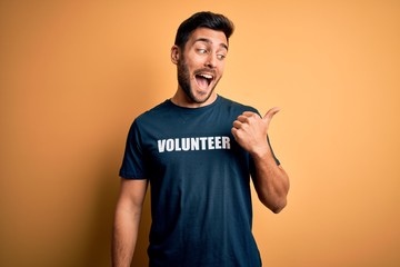 Young handsome man with beard volunteering wearing t-shirt with volunteer message pointing and...