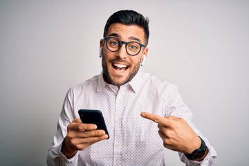 Young handsome man wearing glasses having conversation using smartphone and earphones very happy pointing with hand and finger