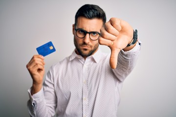 Young business man holding credit card over isolated background with angry face, negative sign...