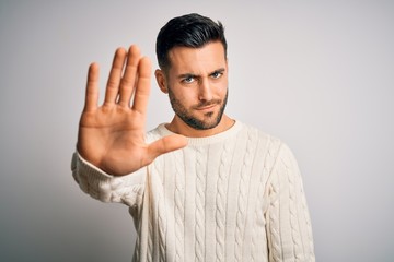 Young handsome man wearing casual sweater standing over isolated white background doing stop sing...