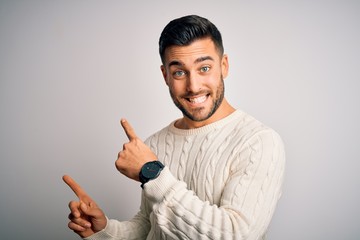 Young handsome man wearing casual sweater standing over isolated white background smiling and looking at the camera pointing with two hands and fingers to the side.