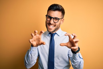 Young handsome businessman wearing tie and glasses standing over yellow background smiling funny...