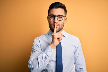 Young handsome businessman wearing tie and glasses standing over yellow background asking to be...