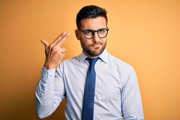 Young handsome businessman wearing tie and glasses standing over yellow background Shooting and...