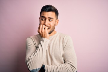 Young handsome man wearing casual sweater standing over isolated pink background looking stressed and nervous with hands on mouth biting nails. Anxiety problem.