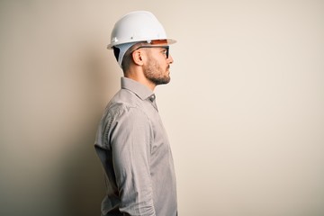 Young architect man wearing builder safety helmet over isolated background looking to side, relax...