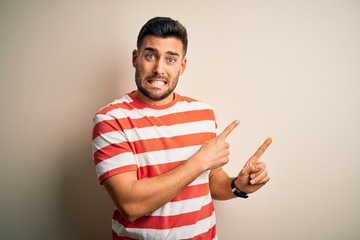 Young handsome man wearing casual striped t-shirt standing over isolated white background Pointing aside worried and nervous with both hands, concerned and surprised expression
