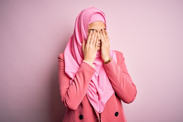 Young beautiful girl wearing muslim hijab standing over isolated pink background rubbing eyes for...