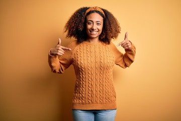 Young african american woman with afro hair wearing casual sweater over yellow background looking confident with smile on face, pointing oneself with fingers proud and happy.