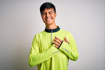 Young handsome sportsman doing sport wearing sportswear over isolated white background smiling with hands on chest with closed eyes and grateful gesture on face. Health concept.