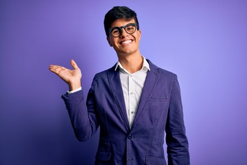 Young handsome business man wearing jacket and glasses over isolated purple background smiling cheerful presenting and pointing with palm of hand looking at the camera.