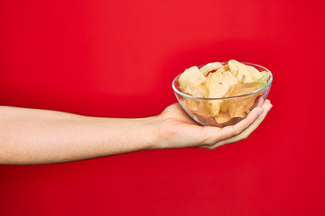 Beautiful hand of man holding bowl with chips potatoes over isolated red background