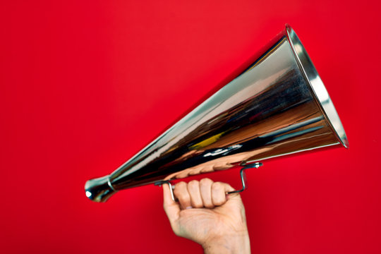 Beautiful hand of man holding vintage megaphone over isolated red background