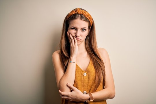 Young beautiful redhead woman wearing casual t-shirt and diadem over yellow background thinking looking tired and bored with depression problems with crossed arms.