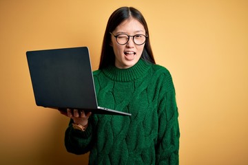 Young asian business woman wearing glasses and working using computer laptop winking looking at the...