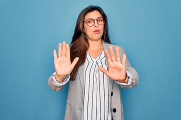Young hispanic business woman wearing glasses standing over blue isolated background Moving away...