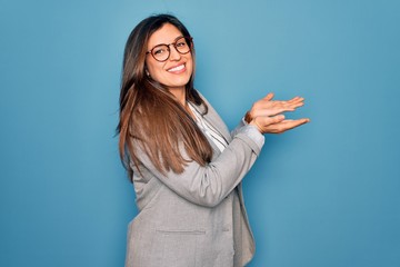 Young hispanic business woman wearing glasses standing over blue isolated background pointing aside...