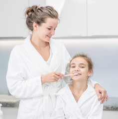 Smiling woman helps her young daughter brush teeth with toothbrush