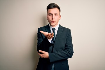 Young handsome business man wearing elegant suit and tie over isolated background looking at the camera blowing a kiss with hand on air being lovely and sexy. Love expression.