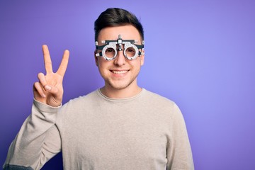 Naklejka premium Young handsome caucasian man wearing optometrical glasses over purple background smiling with happy face winking at the camera doing victory sign. Number two.